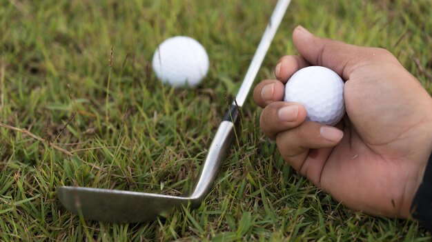 Hand holding golf ball next to a club