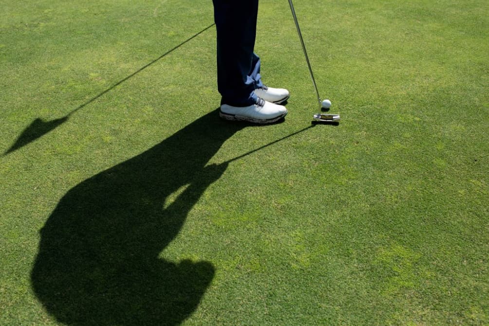 Golfer's shadow on the green while putting a golf ball